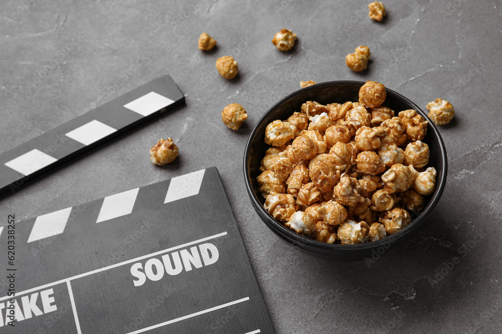 Bowl with tasty popcorn and clapperboard on black background