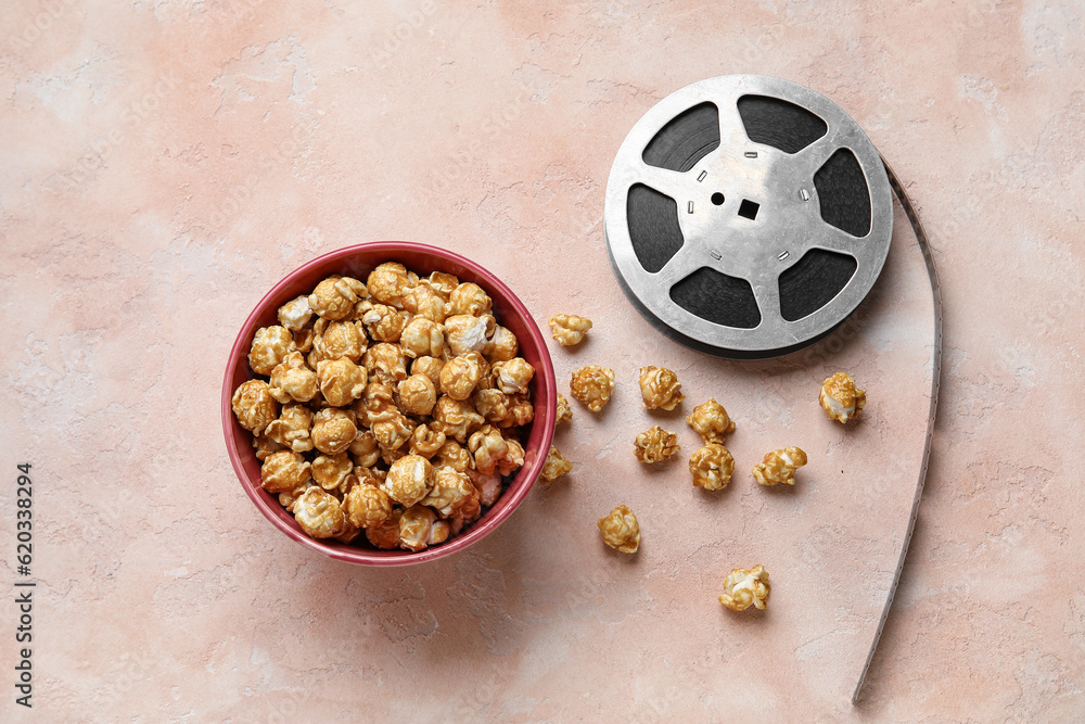 Bowl with tasty popcorn and film reel on pink background