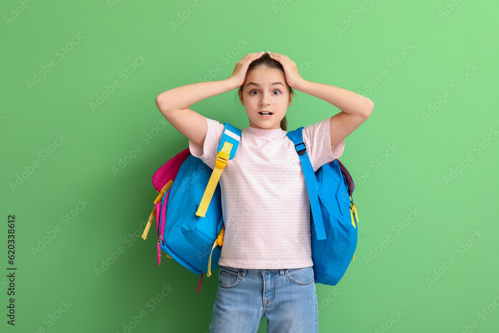 Shocked little girl with backpacks on green background