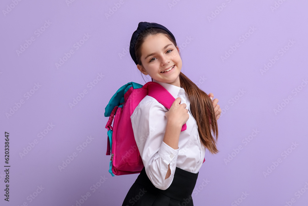 Little schoolgirl with backpack on lilac background