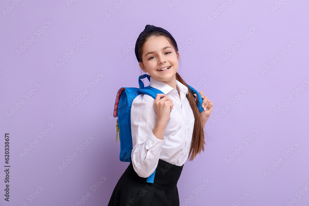 Little schoolgirl with backpack on lilac background