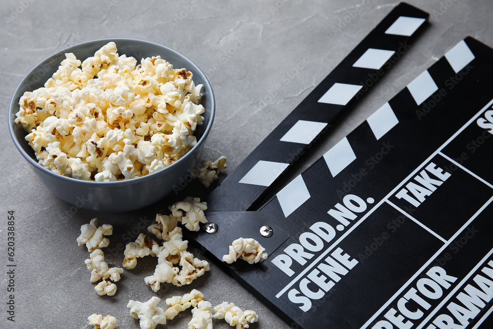 Bowl with tasty popcorn and clapperboard on grey background