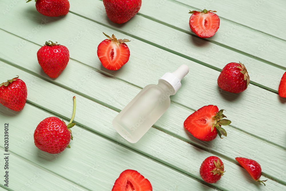 Bottle with cosmetic oil and strawberries on green wooden background