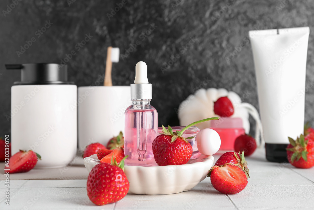 Different cosmetic products and strawberries on white tile table