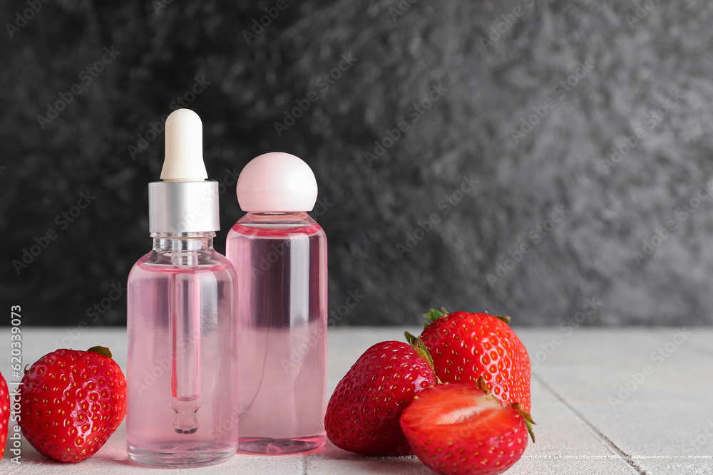 Bottles with cosmetic oil and strawberries on white tile table