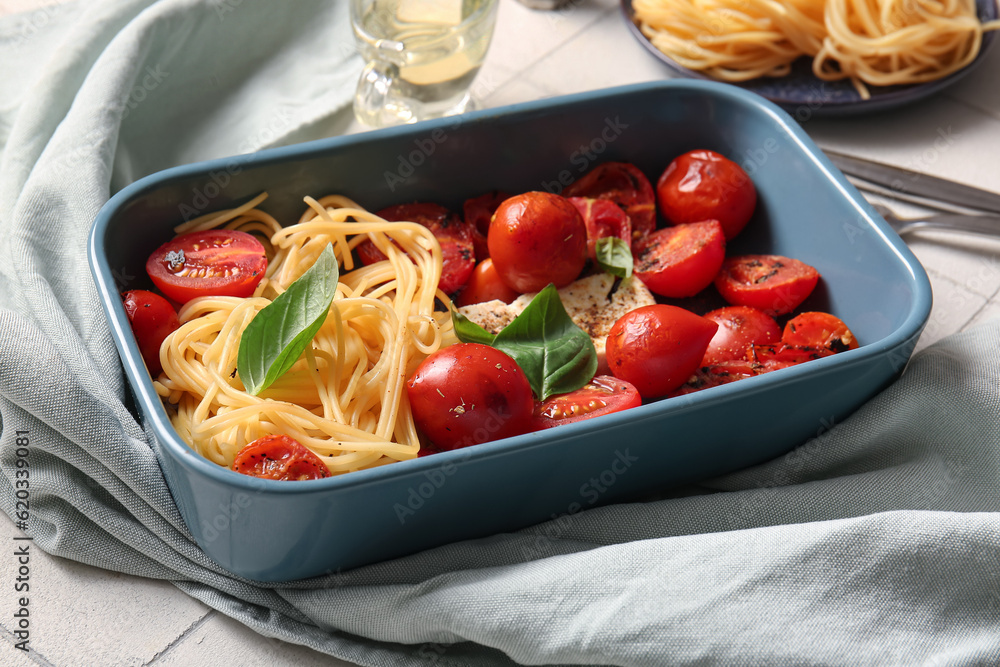 Baking dish of tasty pasta with tomatoes and feta cheese on white tile background