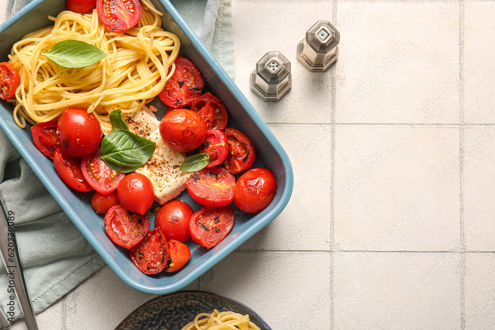 Baking dish of tasty pasta with tomatoes and feta cheese on white tile background