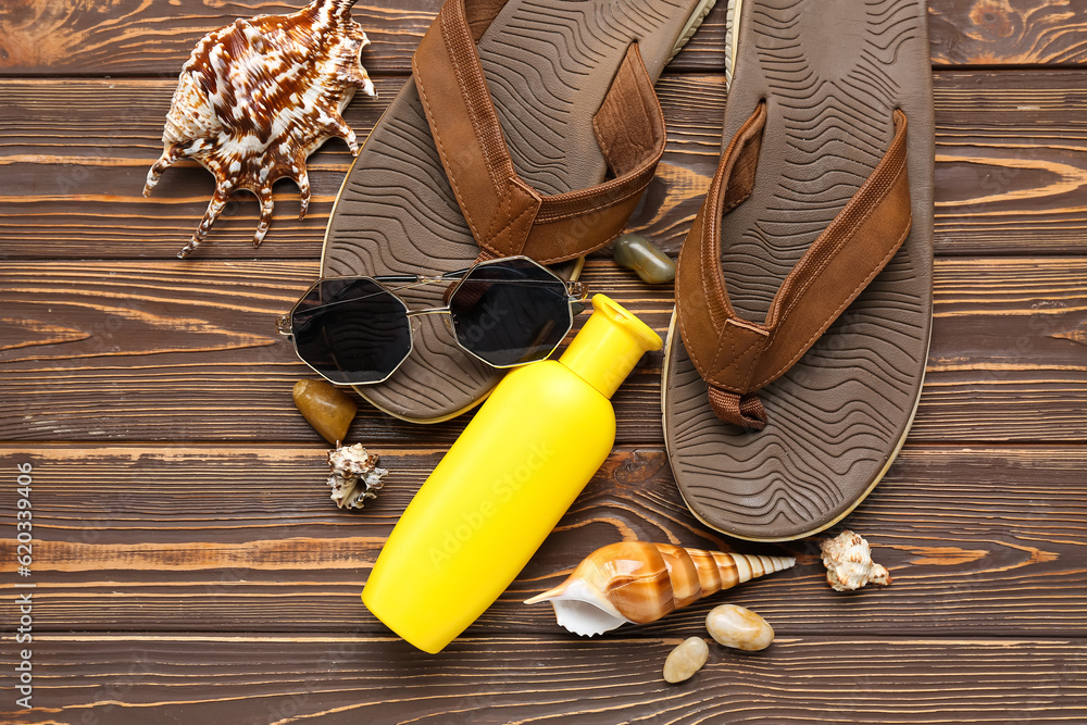 Flip flops with sunglasses, seashells and bottle of sunscreen cream on wooden background