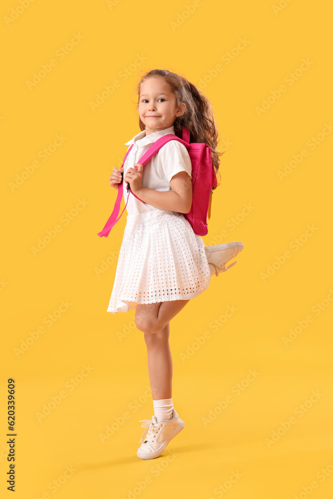 Jumping little schoolgirl on yellow background