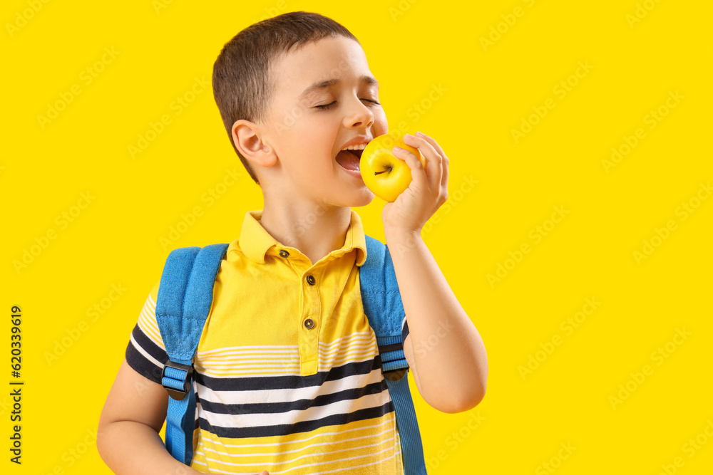 Little schoolboy eating apple on yellow background