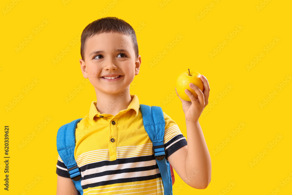 Little schoolboy with apple on yellow background