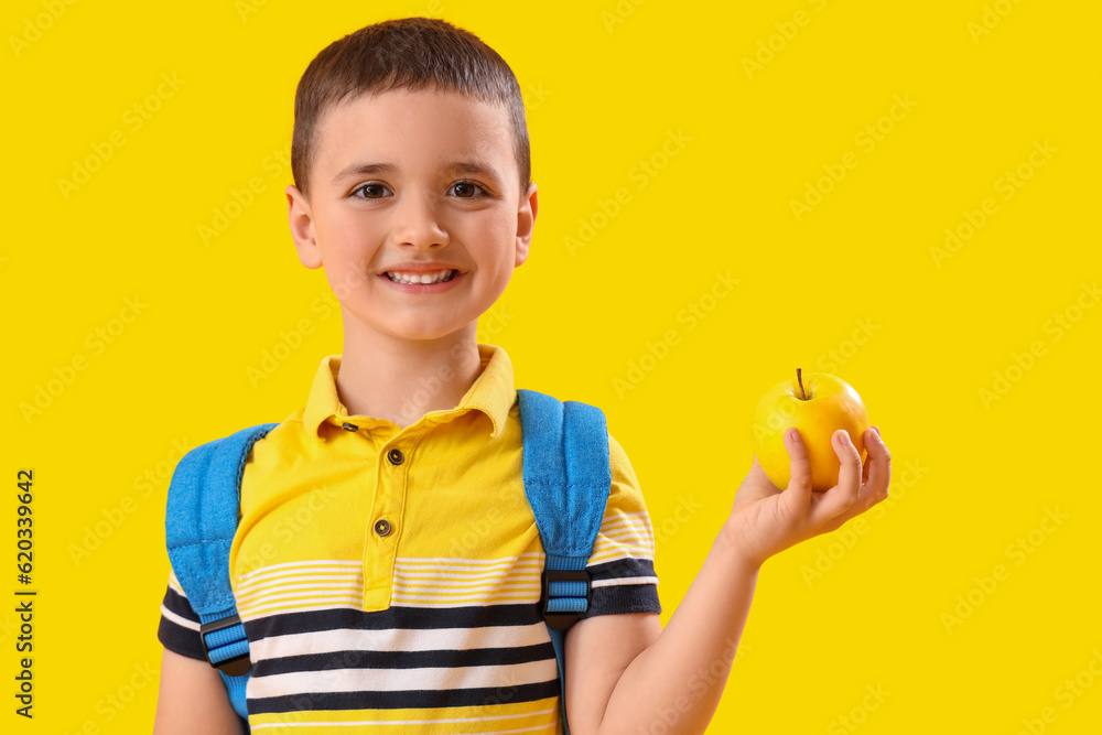 Little schoolboy with apple on yellow background