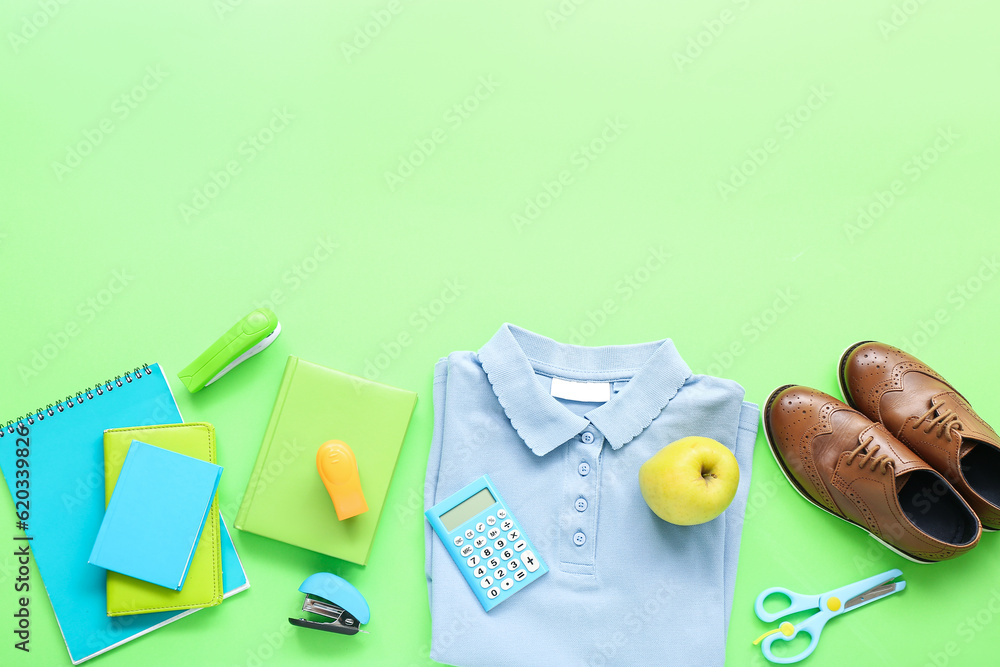 Stylish school uniform with fresh apple and stationery on green background