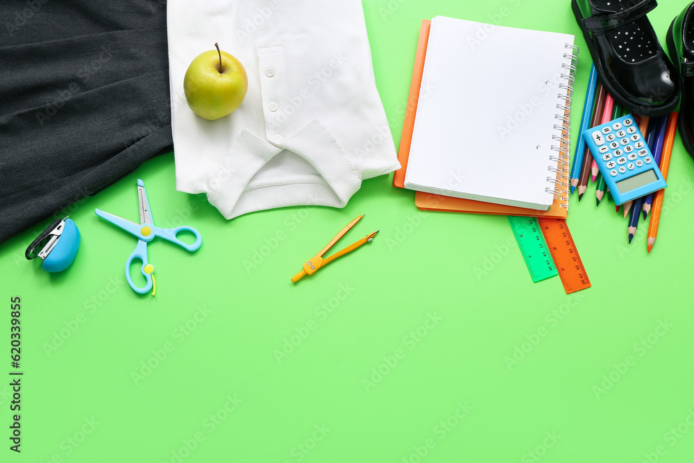 Stylish school uniform with fresh apple and stationery on green background