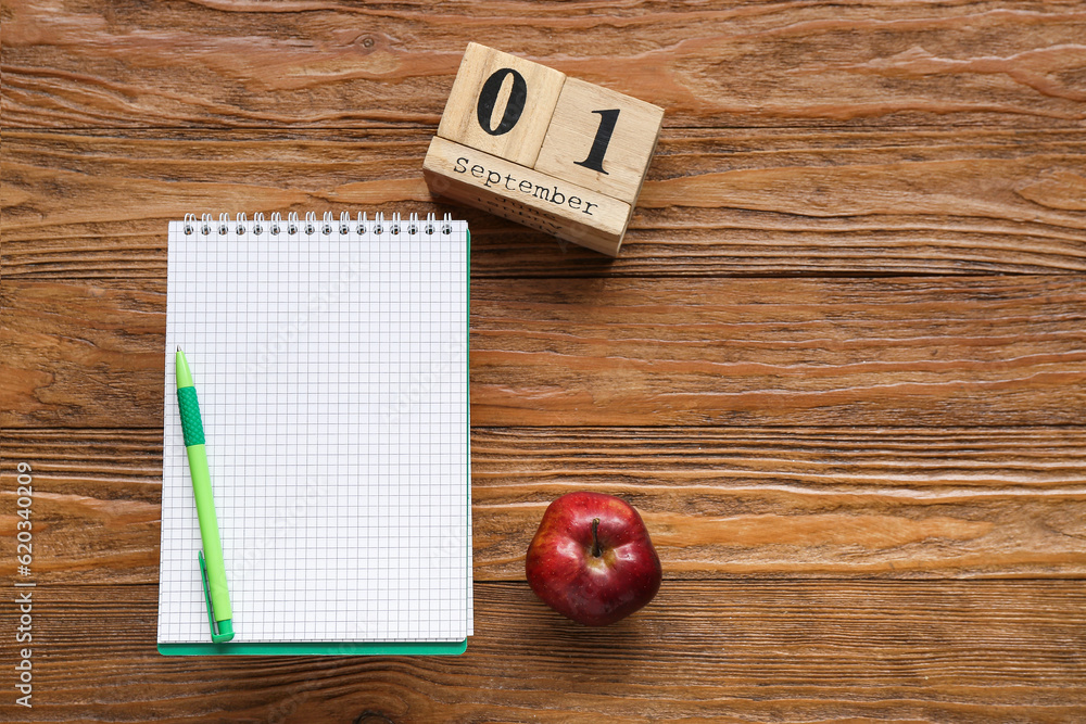 Blank notebook, fresh apple and calendar with date SEPTEMBER 1 on brown wooden background