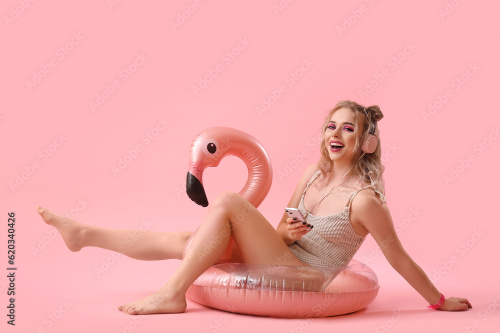 Young woman in swimsuit with mobile phone and inflatable ring on pink background