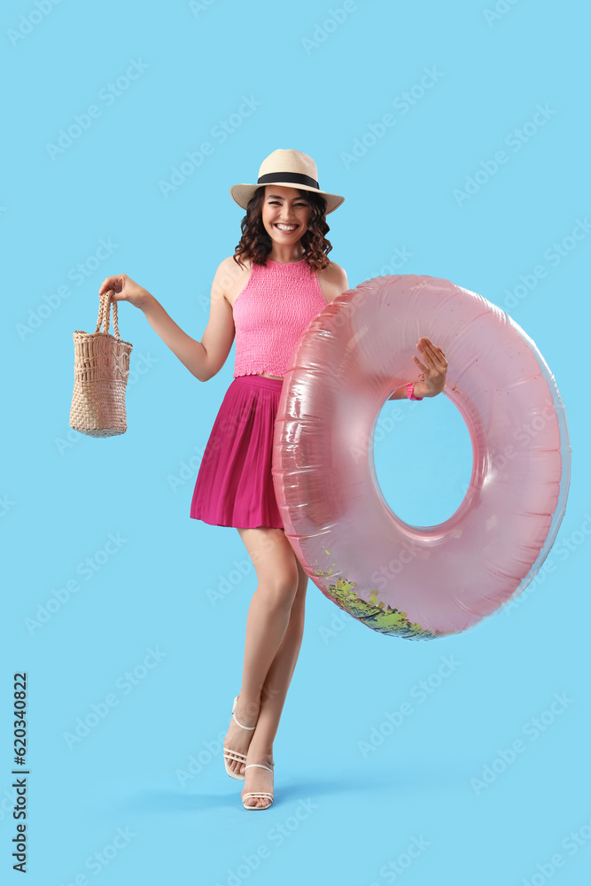 Young woman with beach bag and inflatable ring on blue background