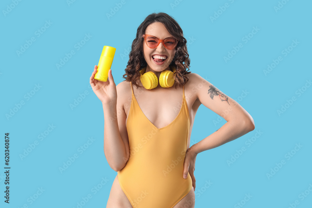 Young woman in swimsuit with sunscreen cream on blue background