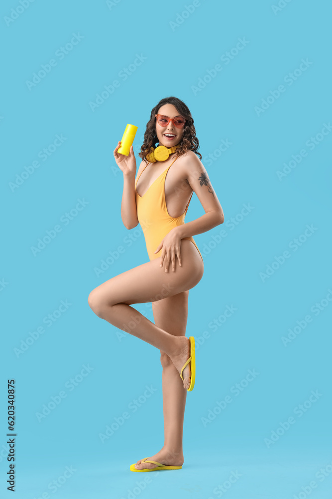 Young woman in swimsuit with sunscreen cream on blue background