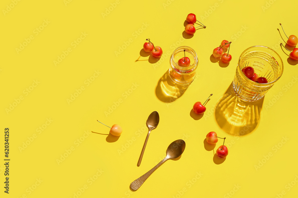 Glass and jar with sweet cherries on yellow background