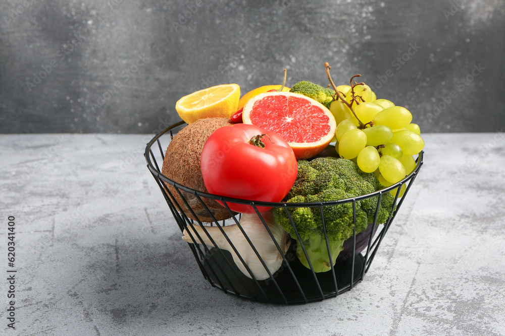 Basket with different fresh fruits and vegetables on grey table