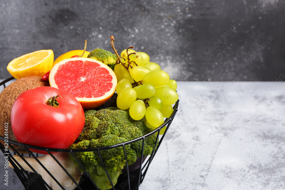 Basket with different fresh fruits and vegetables on grey table