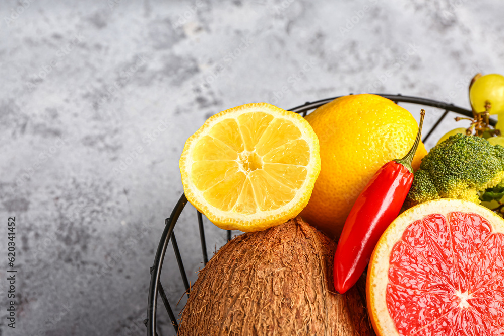 Basket with different fresh fruits and vegetables on grey background, closeup