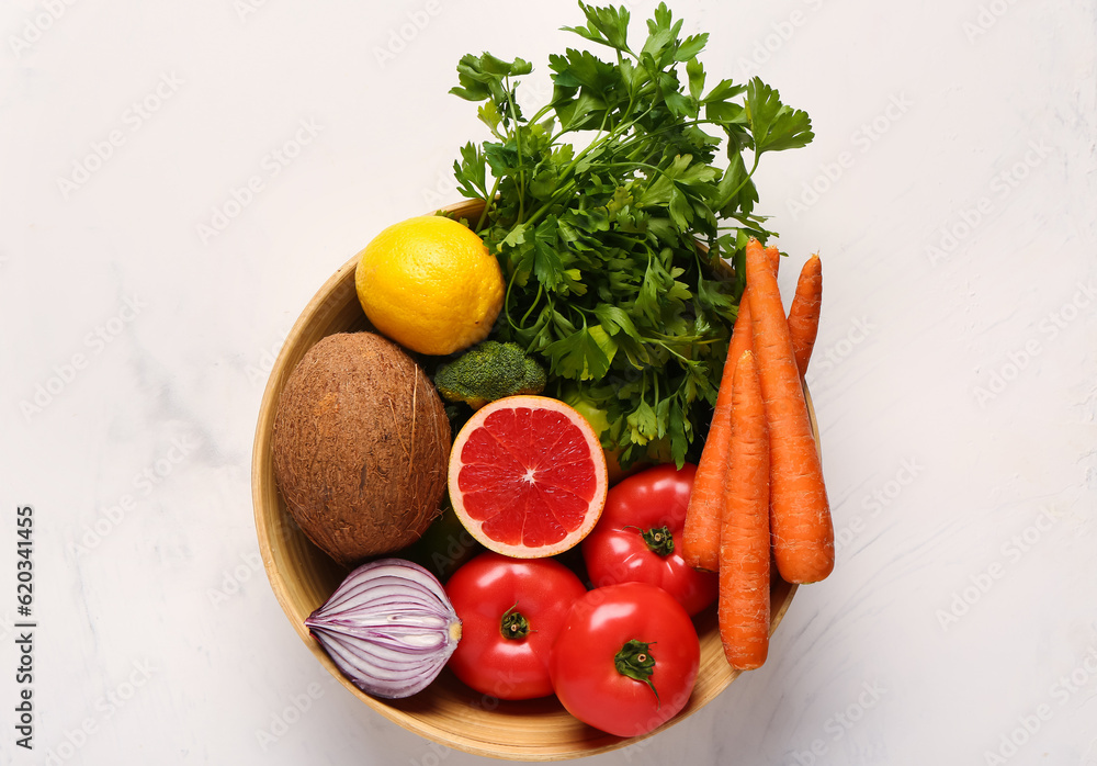 Bowl with different fresh fruits and vegetables on white background