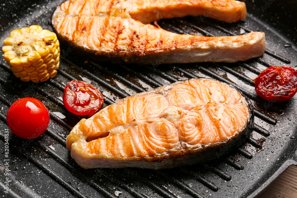 Tasty grilled salmon steaks with vegetables in frying pan, closeup