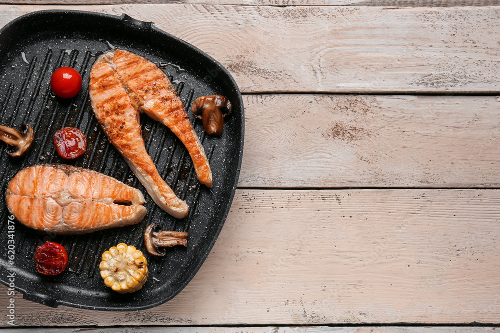 Frying pan with tasty grilled salmon steaks and vegetables on light wooden background