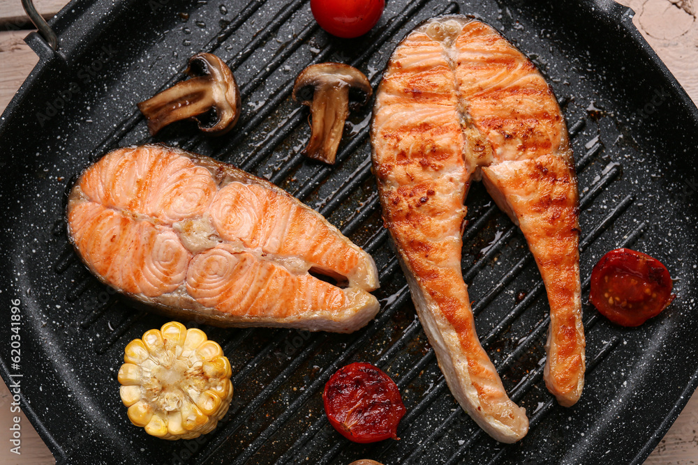 Frying pan with tasty grilled salmon steaks and vegetables on table