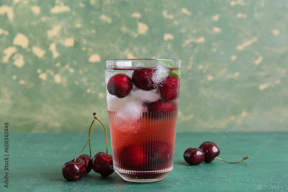 Glass of tasty cherry lemonade on green table