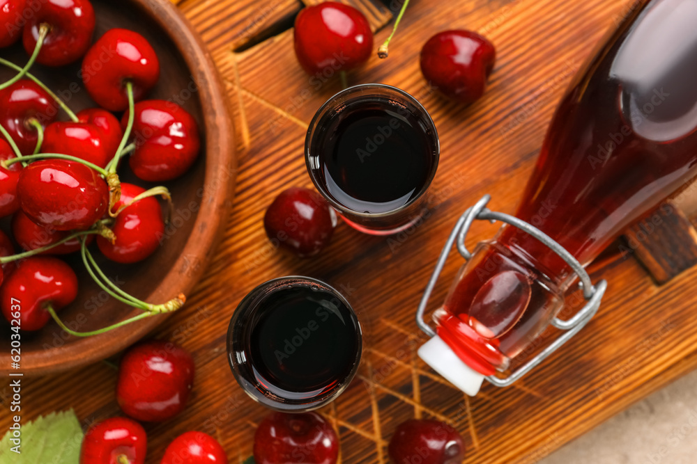 Shots and bottle with sweet cherry liqueur on wooden background, closeup