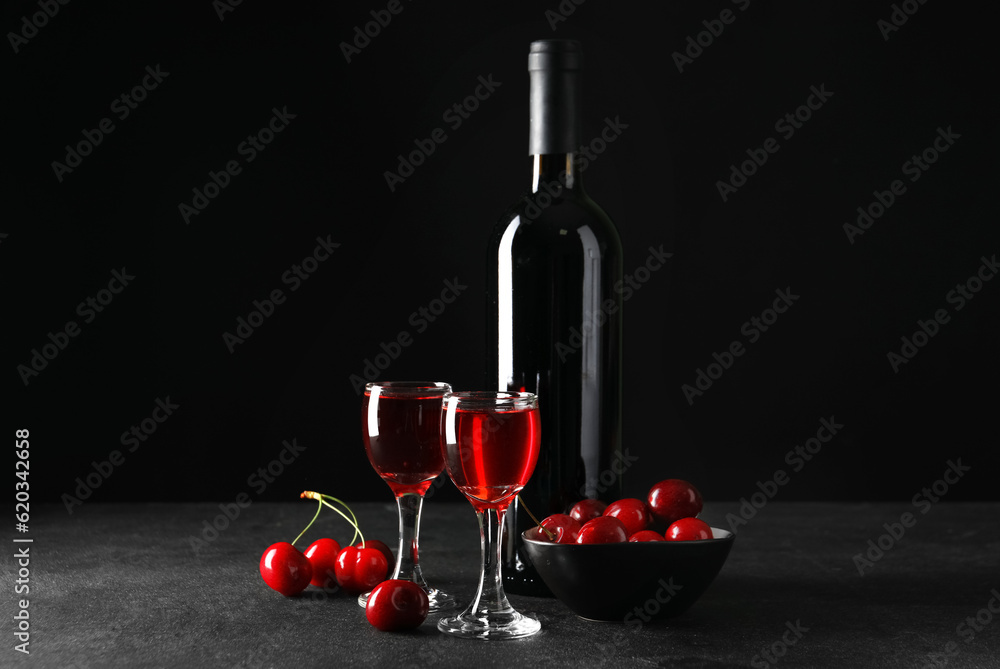 Glasses and bottle with sweet cherry liqueur on black background