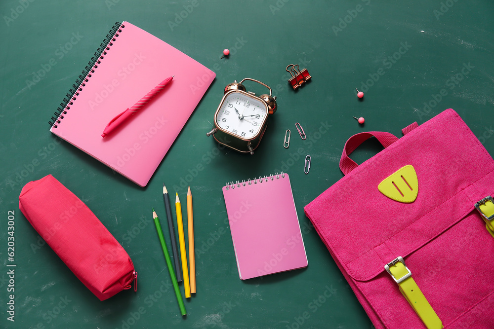 Pink school backpack with notebooks, pencil case and alarm clock on green background