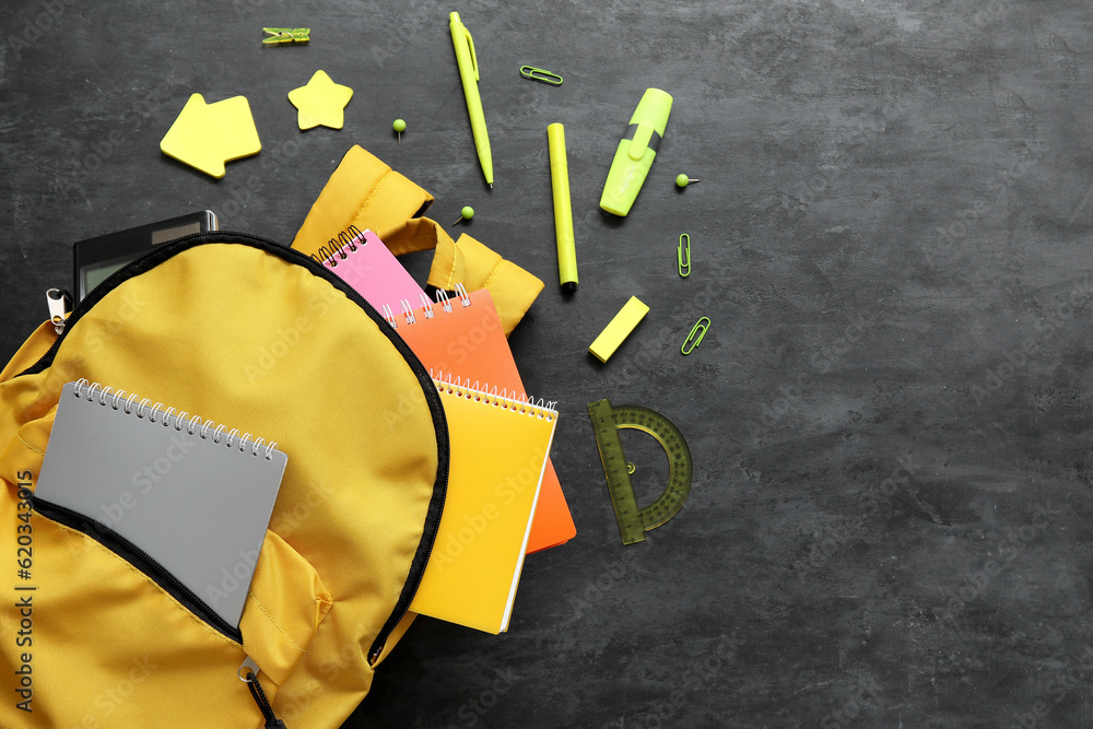 Yellow school backpack with notebooks and different stationery on black background