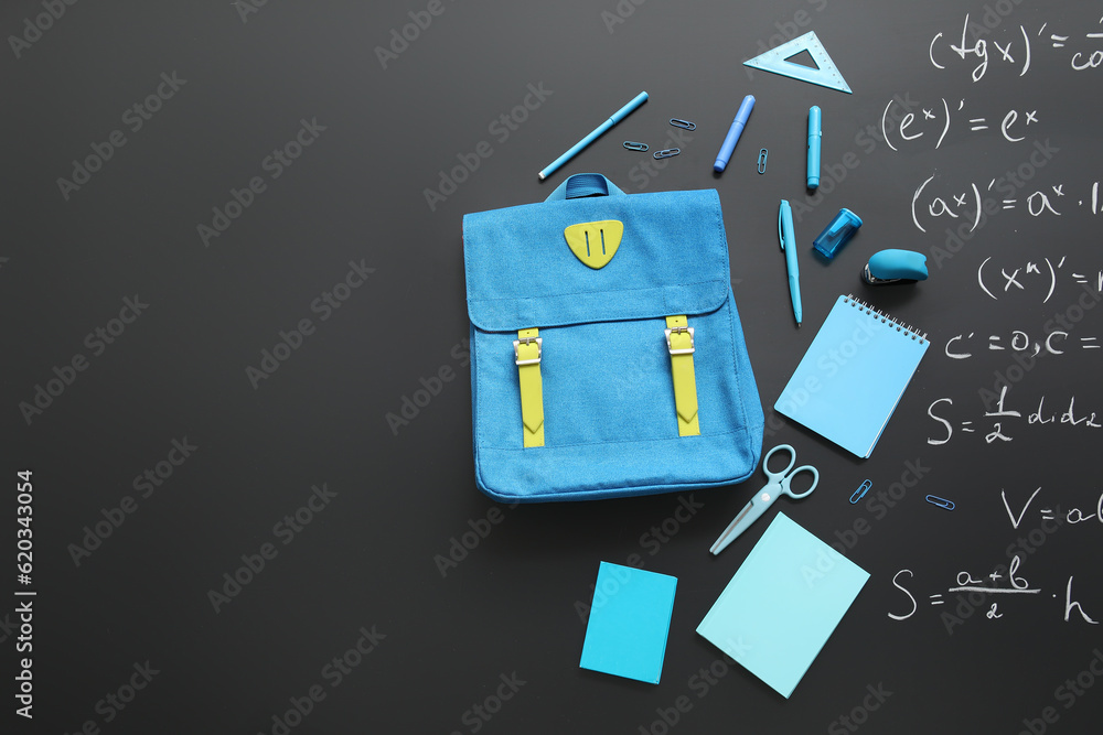 Blue school backpack with different stationery on black chalkboard painted with formulas