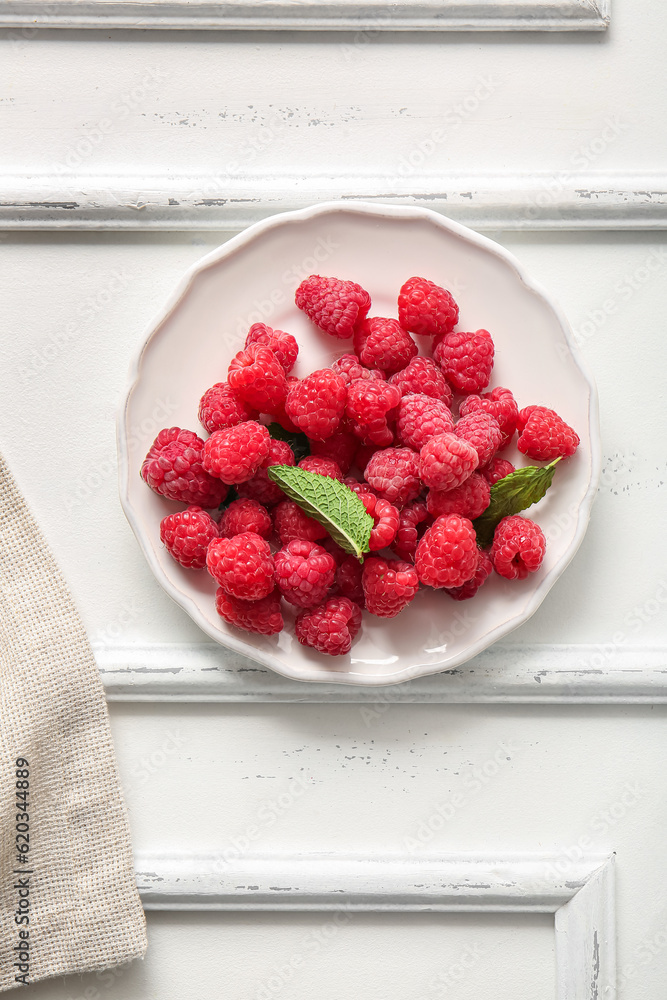 Plate with fresh raspberries and mint on white background