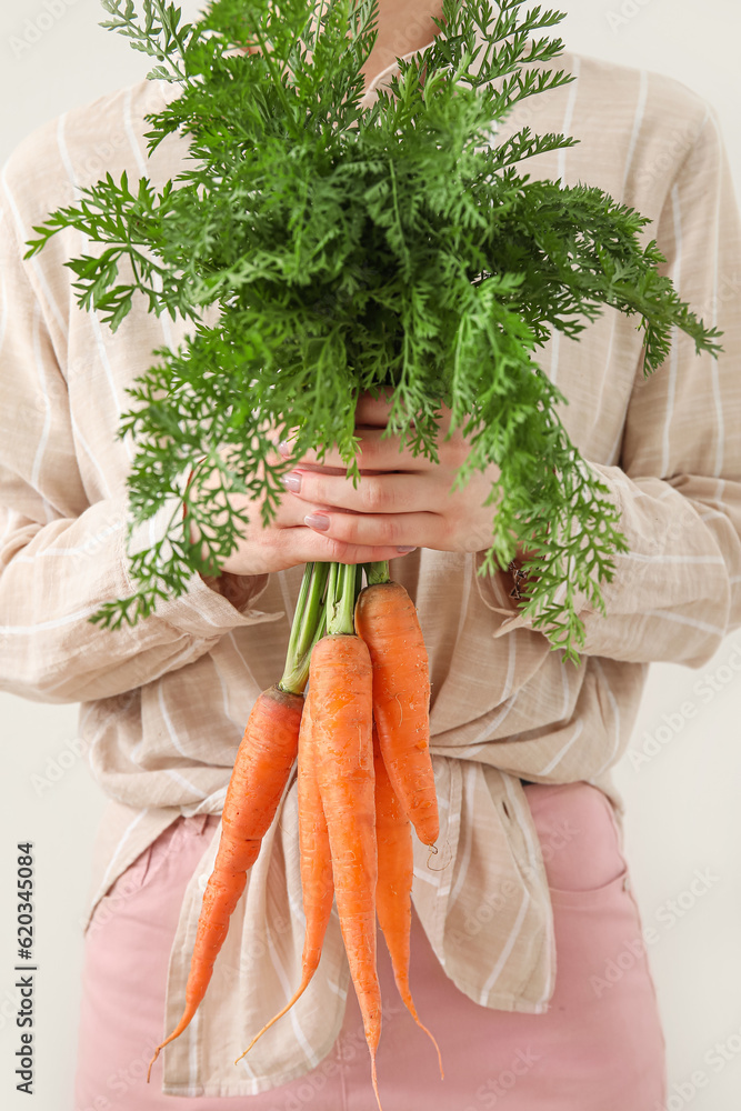 Woman holding bunch of fresh carrots with leaves on light background