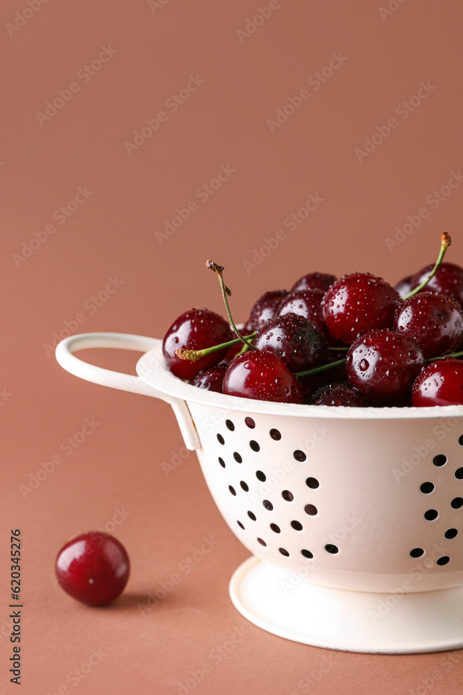 Colander with sweet cherries on brown background