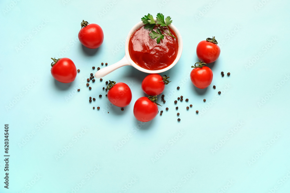 Bowl with tomato paste and fresh vegetables on blue background