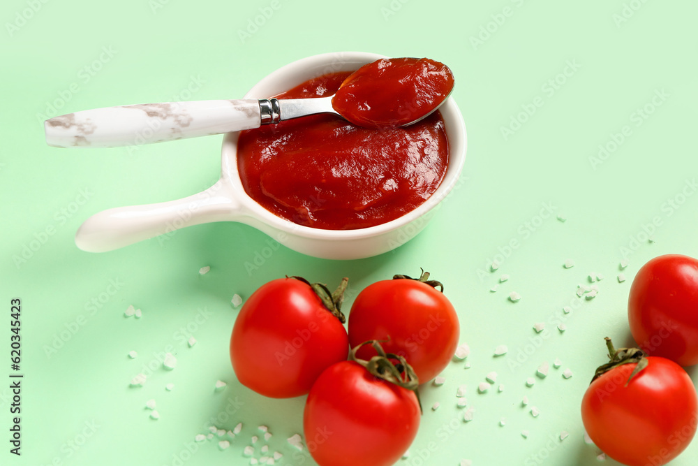 Bowl with tomato paste and fresh vegetables on green background