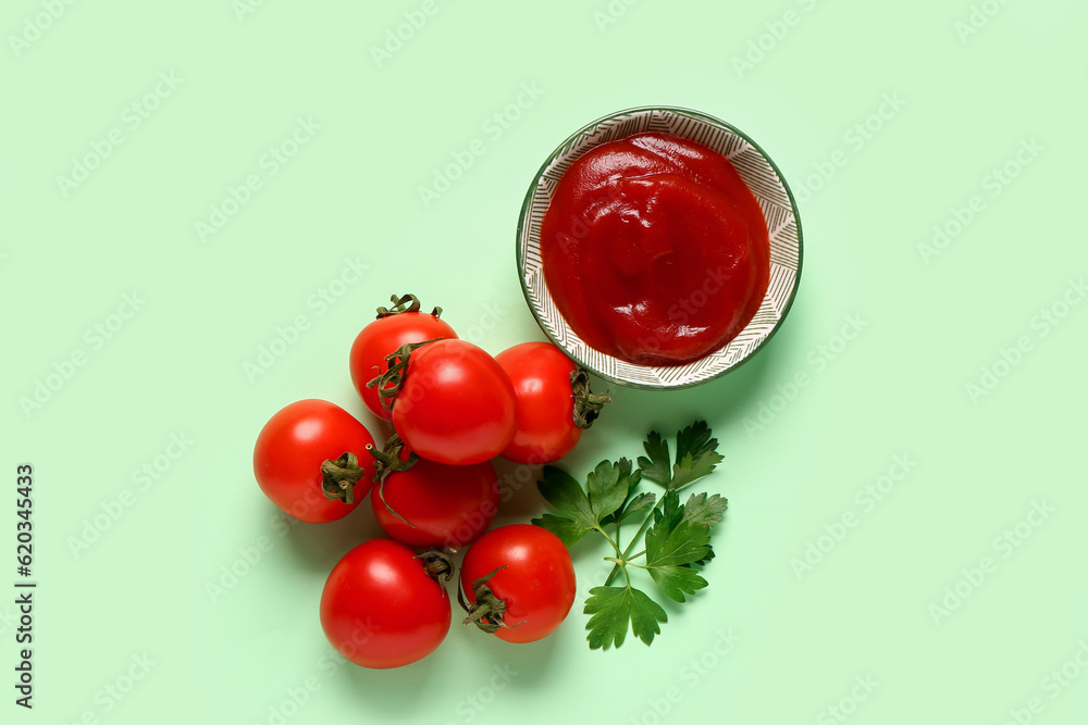 Bowl with tomato paste and fresh vegetables on green background