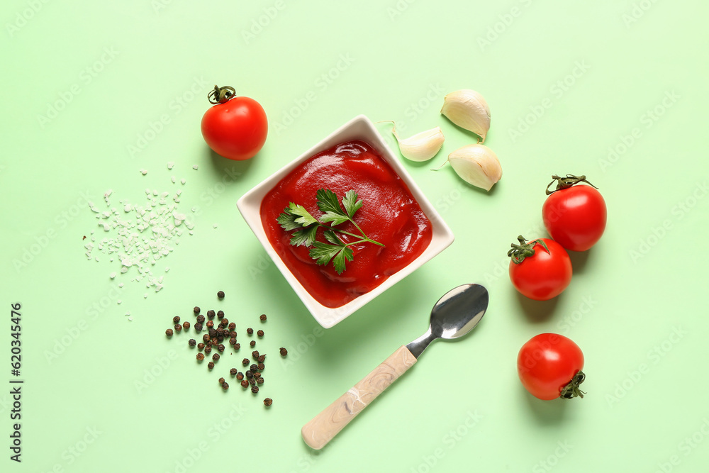 Bowl with tomato paste and fresh vegetables on green background