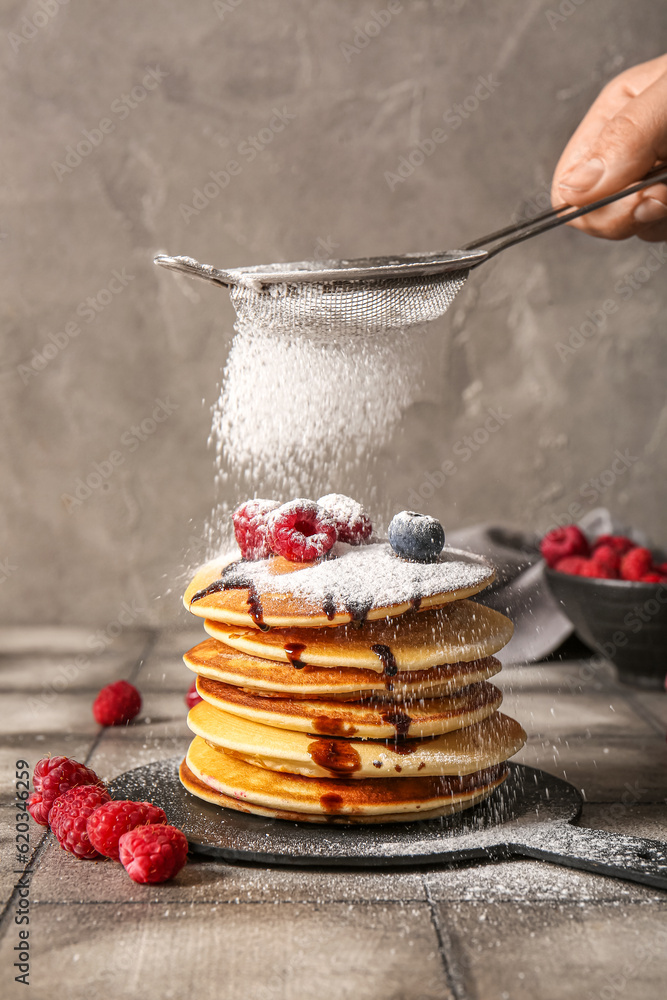 Adding sugar powder onto tasty pancakes with raspberries and blueberries on table