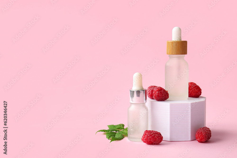 Decorative podium with bottles of cosmetic raspberry oil on pink background