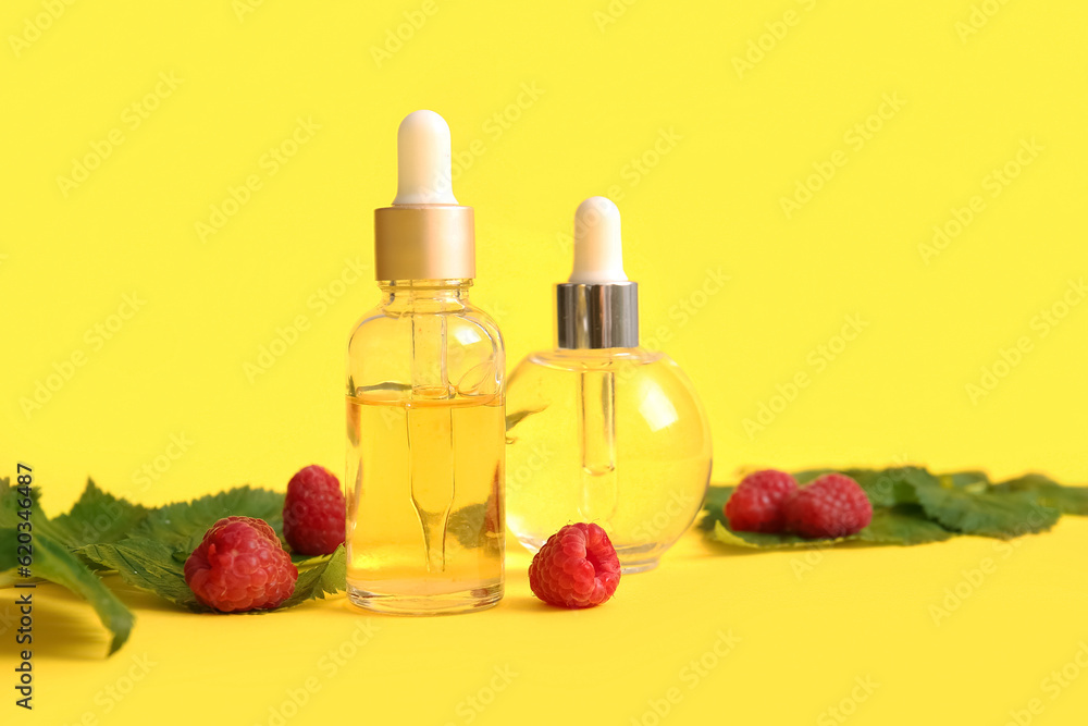 Bottles of cosmetic raspberry oil on yellow background