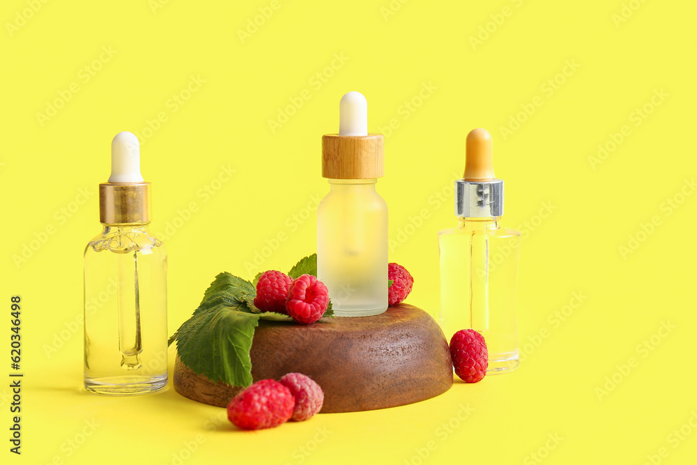 Bottles of cosmetic raspberry oil on yellow background