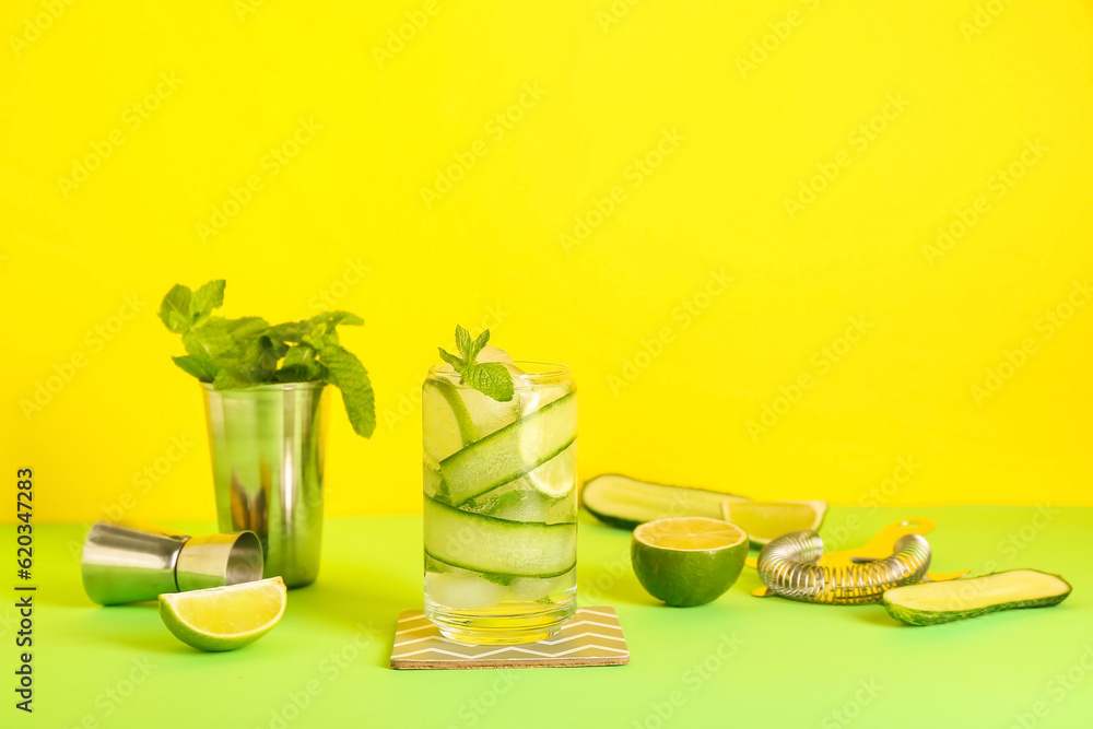 Glass of cucumber mojito with bartender tools on color background