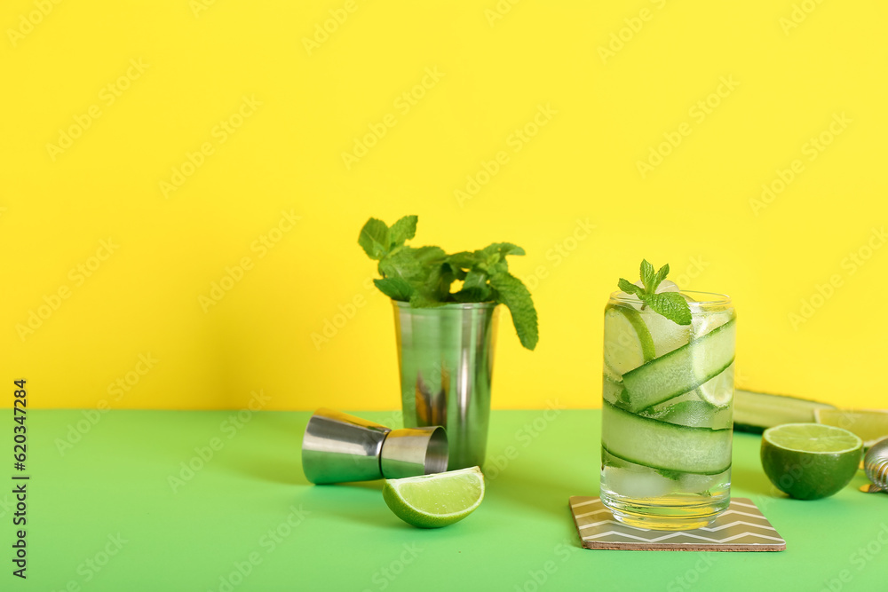 Glass of cucumber mojito with bartender tools on color background